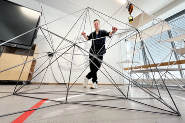 A person leans with his hands on a delicate structure made of metal rods.