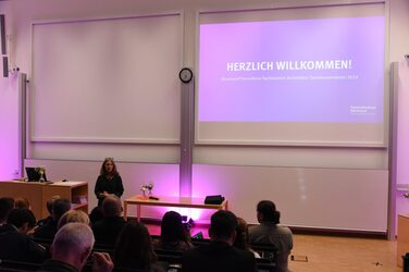 Dean Diana Reichle stands on the stage of the large lecture hall and gives the welcoming speech for the students and their families.