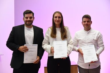 Three students hold up their award from the magazine "wettbewerbe aktuell" for their outstanding achievements.