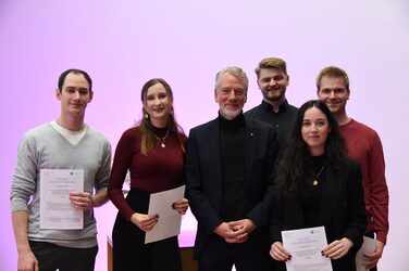 Prof. Helmut Hachul with five students holding their certificates on the stage of the lecture hall.