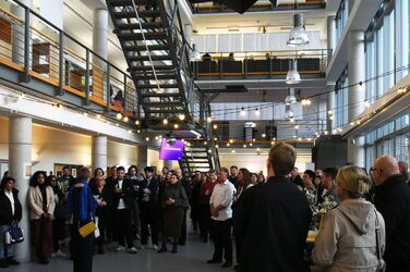 Prof. Christiane Fülscher holds the farewell speech for the graduates in the foyer of the faculty, with the former students and their families standing in the background.