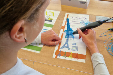 Eine Person erstellt mit einem speziellen Stift ein kleines 3D-Modell des Eiffelturms.