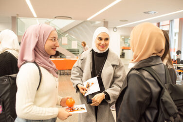 Drei Studentinnen halten ihre Gewinne vom Gewinnspiel des Intertnational Day in den Händen und unterhalten sich lächelnd.Three students hold their prizes from the Intertnational Day competition in their hands and chat with smiles on their faces.