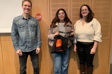 Preisübergabe an eine Teilnehmerin des Gewinnspiels: Ein Mitarbeiter des International Office und eine Mitarbeiterin der Auslandsgesellschaft überreichen der Gewinnerin eine gefüllte Stofftasche
The winner of the stamp rallye receives her prize: Employees of the International Office and Auslandsgesellschaft hand out a filled tote bag to a young female student