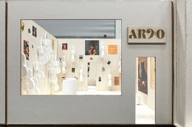 Front of a miniature model of a cello store called "Arco". Through the doorway and shop window, white cellos can be seen on the walls inside, in between pictures with classical-looking motifs.