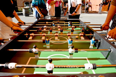 View of a foosball table from diagonally above, hands reach for the control rods from the left and right.