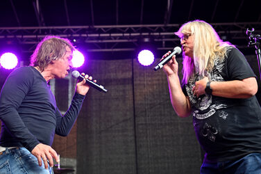 Two people on a stage sing into their microphones facing each other.