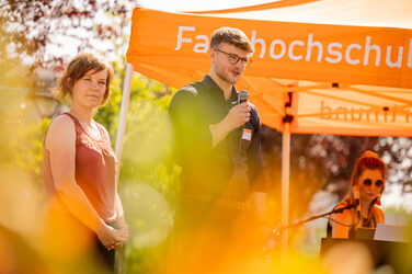 PhD students speak on stage in summery weather