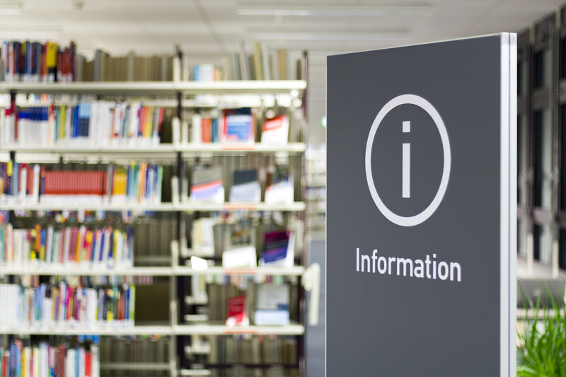 Photo of a sign reading "Information" with a library book shelf in the background__Photo of a sign reading "Information" with a library book shelf in the background