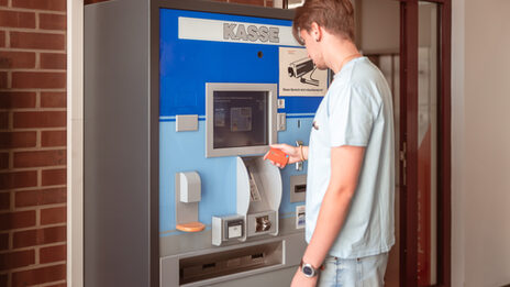 Photo of a young man operating the ticket machine in front of the library.