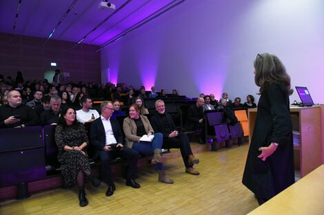 View from the stage into the purple illuminated large lecture hall with the audience in the background.