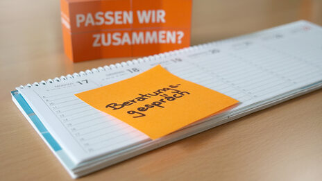 Photo of a desk calendar with an orange Post-It with the note "Counseling interview" stuck to it. In the background are stacked cubes with the words "Are we a match?" written on them.