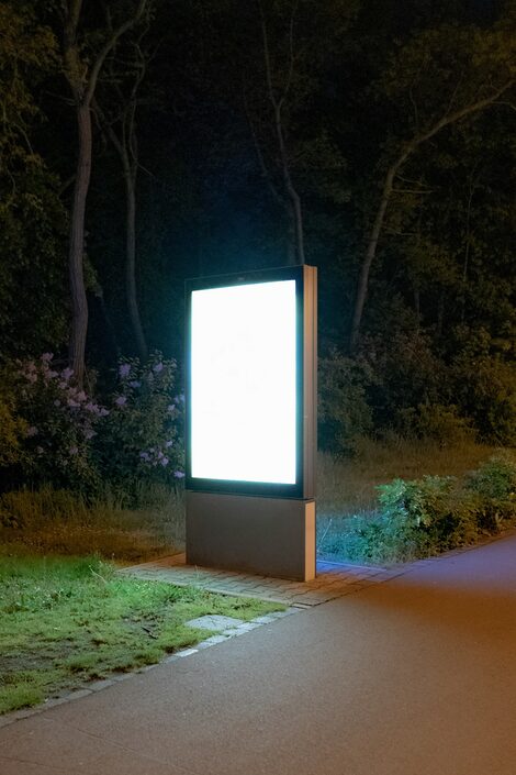 An advertising display lights up in front of a dark wooded area.