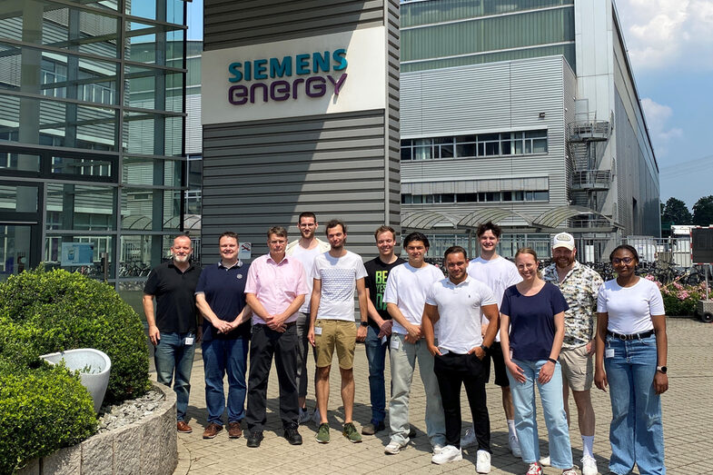 Twelve people stand in front of a building with Siemens Energy lettering above them.