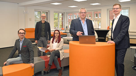 A group of people stand and sit at and around an orange desk in the User Innovation Center.