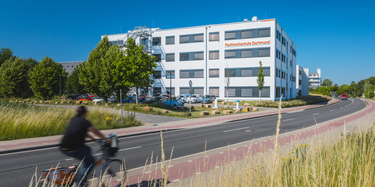 Gebäudeaufnahme mit Logoanbringung "Fachhochschule Dortmund" am Gebäude 38b - aus der Ferne. Fahrradfahrer fährt links ins Bild.