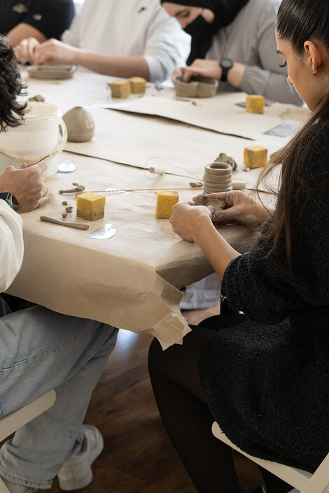 At a table, people make sculptures out of clay with the help of tools.