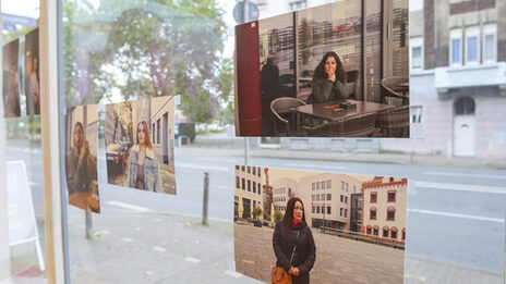 Auf einer Fensterscheibe sind mehrere Fotos angebracht. Die Fotos sind Teil der Ausstellung und zeigen die Gesichter geflüchteter Frauen, die jetzt in Deutschland leben.