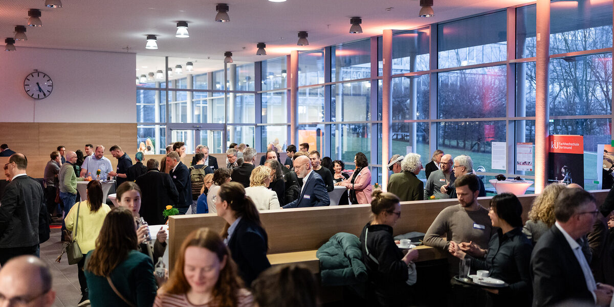 Menschen in einem Foyer, einige sprechen miteinander in kleinen Gruppen, andere schauen sich um.