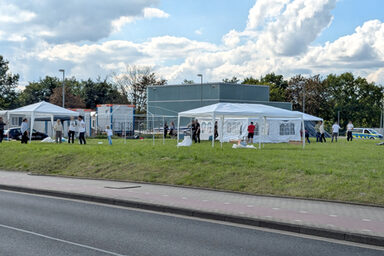 Menschen bauen auf einer Wiese Pavillons und Zelte auf.