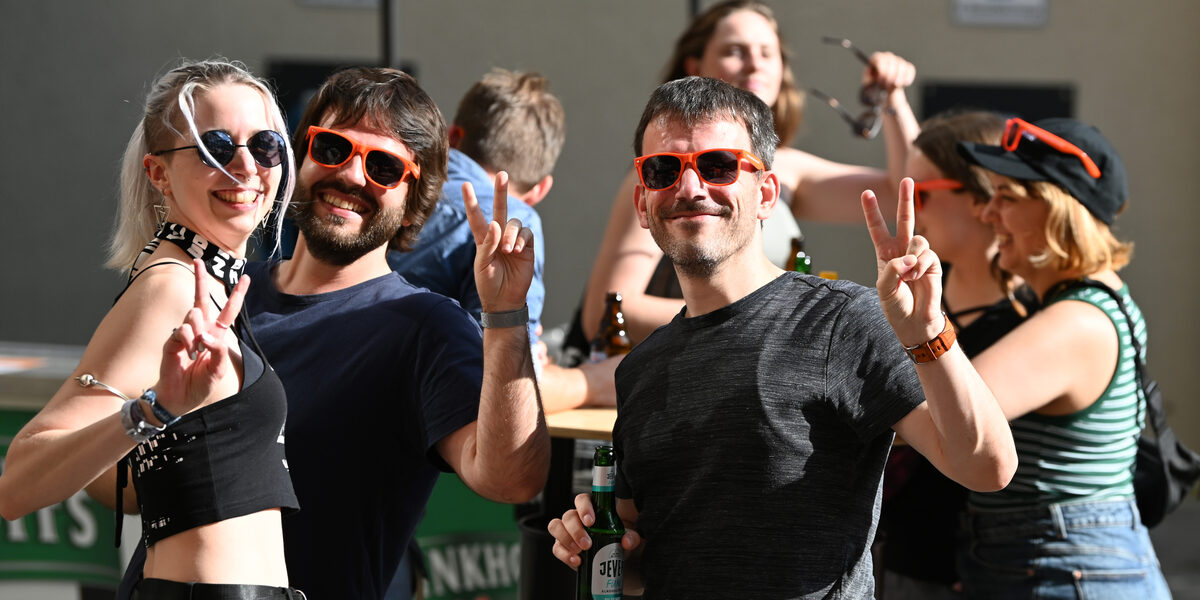 Several people, some wearing orange sunglasses, smile and greet the camera with V-signs.