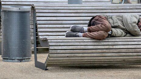 A homeless person lies on a bench