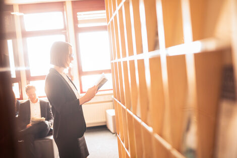 Photo of a doctoral student standing in front of a bookshelf in the library and reading a book.