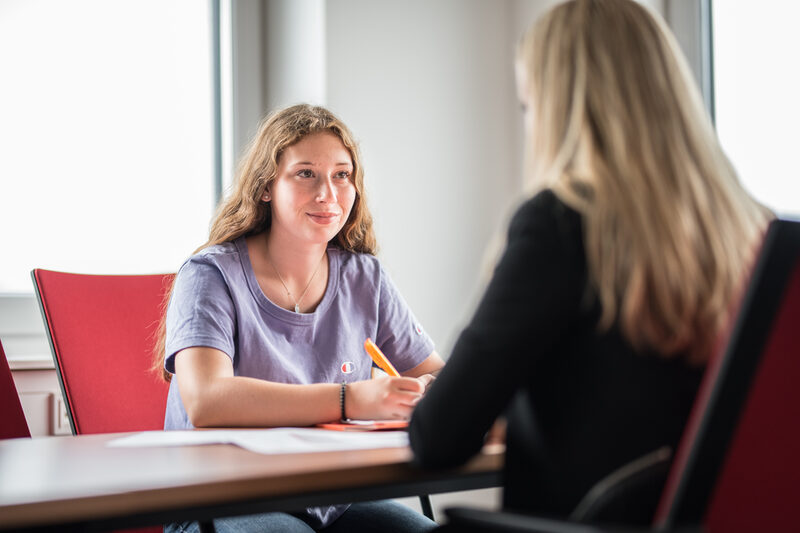 Photo of a student sitting opposite another woman, who can only be seen in the crop on the right of the picture. They are having a student counseling interview.