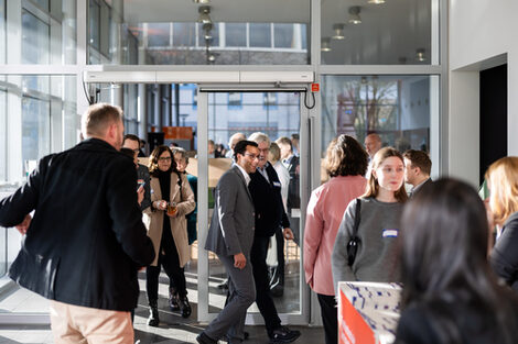 Menschen in einem Foyer, einige sprechen miteinander in kleinen Gruppen, andere schauen sich um.