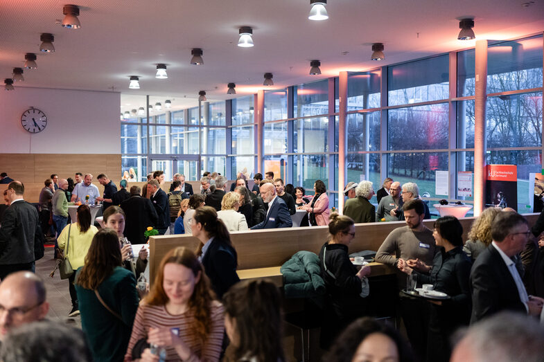 Menschen in einem Foyer, einige sprechen miteinander in kleinen Gruppen, andere schauen sich um.