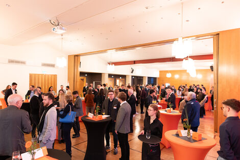 In a large room, several people are standing at tables and chatting.