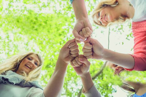 Photo from the frog's perspective: Four people holding their fists together. The face of two of the people can be seen.