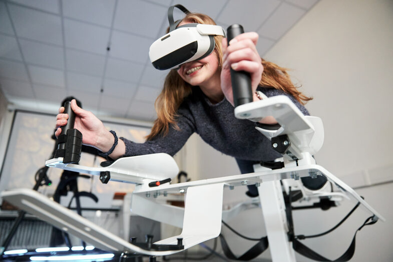 Photo of a person on the Icaros device. She is wearing VR goggles and holding on to the handles.